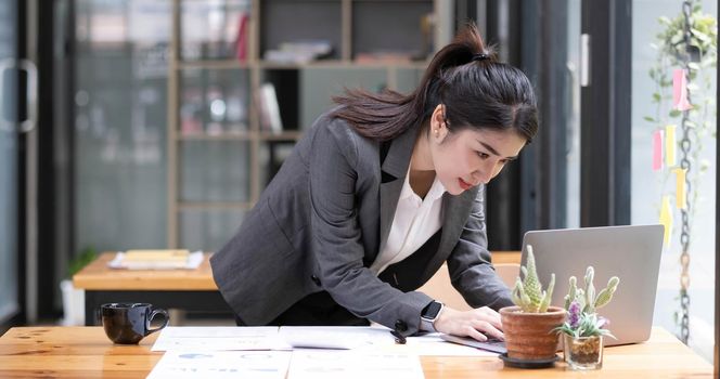 Happy attractive Asian business woman working with a laptop and financial document at office, successful action, Business concept..