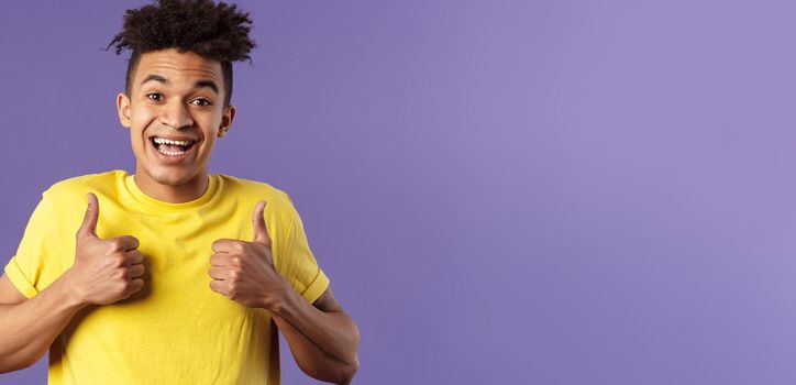 Close-up portrait of enthusiastic healthy hispanic guy staying positive, show thumbs-up and smiling, encourage people stay home, feel fine, like and approve friends plan, standing purple background.