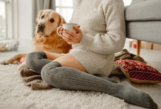 Girl with golden retriever dog sitting on floor with mug with cocoa and marshmallow. Young woman with hot beverage and pet doggy at home