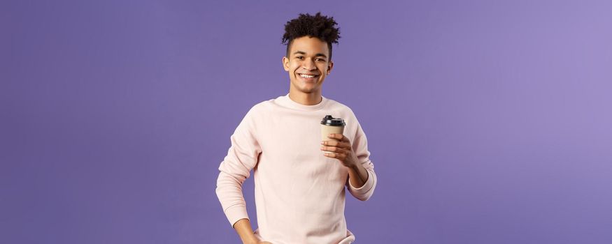 Lifestyle, cafe, eating-out concept. Portrait of cheerful young hispanic guy holding take-away cup of coffee, drinking and smiling camera, waiting for someone, thanking coworker for bringing cappucino.