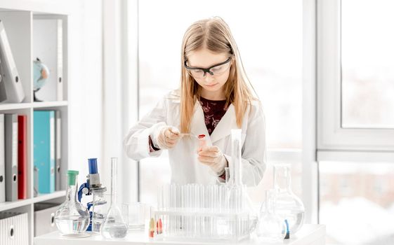 Smart girl doing scientific chemistry experiment wearing protection glasses. Preteen schoolgirl with equipment and chemical liquids on school lesson