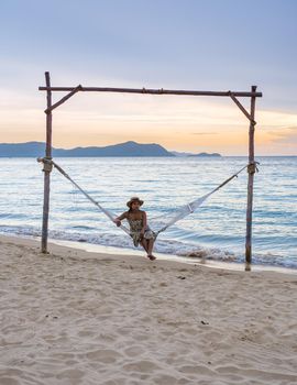 Men and women watching the sunset in a hammock on the Pattaya beach during sunset in Thailand Ban Amphur beach. couple walking on a tropical beach with palm tree and hammock during sunset