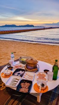 women bbq cooking noodle soup during sunset in Thailand Ban Amphur beach. relaxing with bbq Thai traditional on a tropical beach with palm trees and hammock during sunset