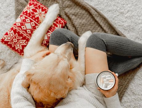 Girl holding mug with cocoa and marshmallow and hugging golden retriever dog in festive holidays time. Young woman with hot beverage and pet doggy at home