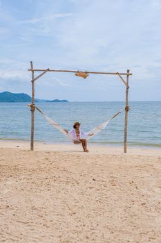 Women on the beach on a sunny day with a hammock on the beach in Pattaya Thailand Ban Amphur beach. Asian women on a tropical beach with palm trees and hammocks