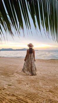 Women are watching the sunset in a hammock on Pattaya beach during sunset in Thailand Ban Amphur beach. Asian women walking on a tropical beach with palm trees and hammocks during sunset