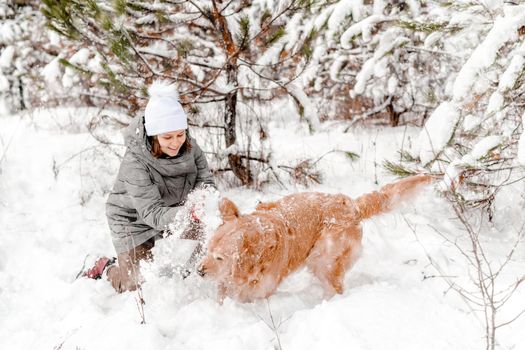 Girl playing with golden retriever dog in snow in winter time and smiling. Young woman with doggy pet outdoors in cold weather with snowflakes