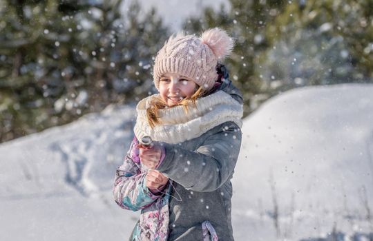 Preteen girl child playing in winter snow time outdoors and smiling. Pretty female kid enjoying cold weather