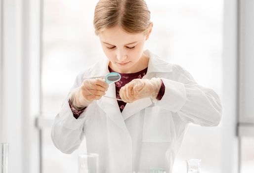 Smart girl during scientific chemistry experiment looking at glass with tests. Schoolgirl with chemical equipment on school lesson