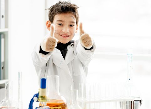 School boy showing super with hands holding big fingers up during chemistry experiment in elementary science class. Clever pupil kid in lab