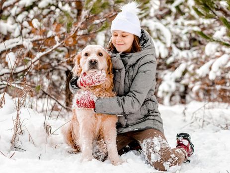 Girl petting and hugging golden retriever dog sitting in snow in winter time. Young woman with doggy pet outdoors in cold weather with snowflakes