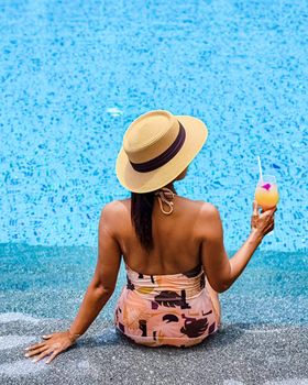 Asian women with a hat relaxing in the swimming pool with a cocktail in hand, women swimming pool banner holiday vacation concept, Asian women in blue swimming pool luxury vacation