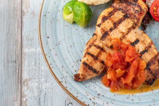 Grilled chicken breast in different variations with cherry tomatoes and different vegetables on wooden background