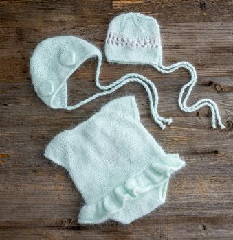 Knitted newborn hats clothes for infant studio photoshoot on wooden background closeup