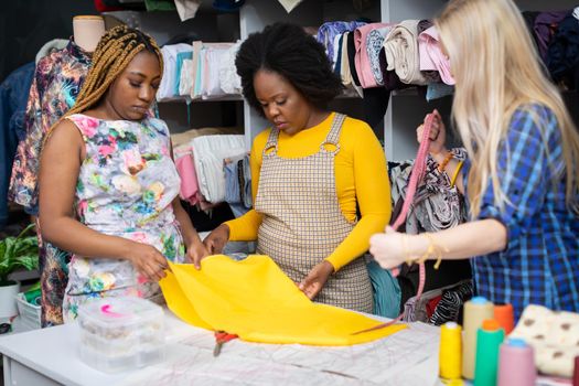 Two dark-skinned ladies are considering buying yellow fabric for a summer dress. The facilities of a creative tailor shop.