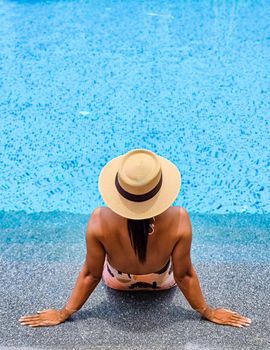 Asian women with a hat relaxing in the swimming pool with a cocktail in hand, women swimming pool banner holiday vacation concept, Asian women in blue swimming pool luxury vacation