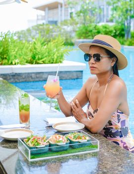 Asian women with a hat relaxing in the swimming pool with a cocktail in hand, women swimming pool banner holiday vacation concept, Asian women in blue swimming pool luxury vacation