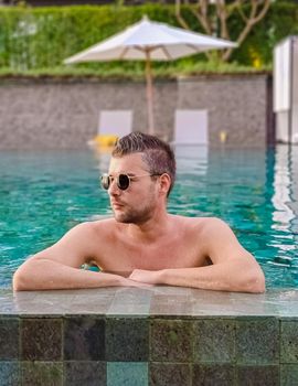 Young men with sunglasses by the pool on a luxury vacation, young caucasian men in the swimming pool