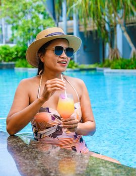 Asian women with a hat relaxing in the swimming pool with a cocktail in hand, women swimming pool banner holiday vacation concept, Asian women in blue swimming pool luxury vacation