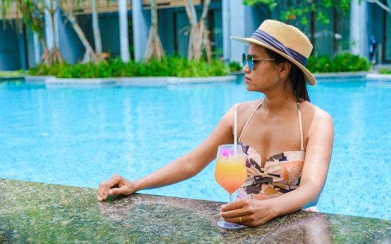 Asian women with a hat relaxing in the swimming pool with a cocktail in hand, women swimming pool banner holiday vacation concept, Asian women in blue swimming pool luxury vacation