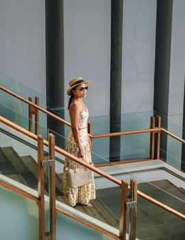 Asian women with a hat walking down from stairs on the back of a grey building during sunset.