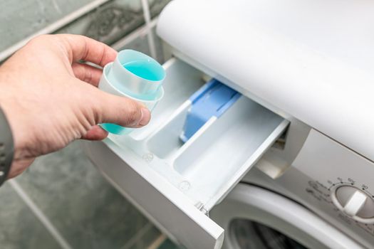 Male hand pouring laundry detergent into washing machine before doing the laundry