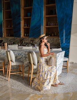 Asian women with a hat relaxing at the bar in a hotel during a luxury vacation. women by the bar during sunset