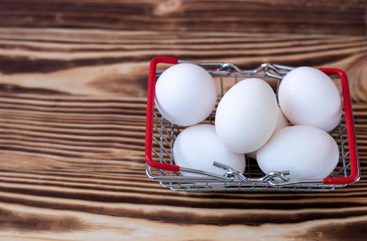 white chicken eggs in a grocery basket stand on a burnt wooden background. Farm products shopping concept. High quality photo