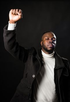 Black man with raised fist, fighting for his rights. Mid shot. Black background.