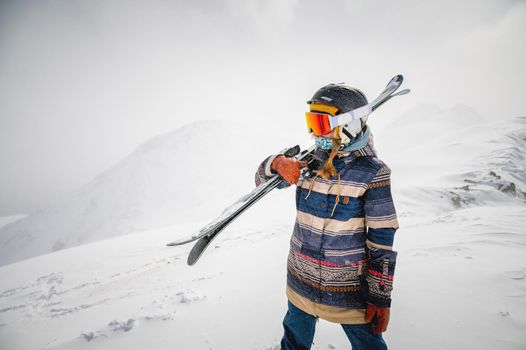 Portrait of a pretty and active woman skier, wearing a mask and holding skis in her hands, active winter holidays. extreme lifestyle concept