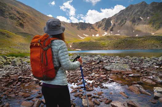 rear view, young woman enjoying mountain lake, tourist looks into distance at rocky peaks of mountain, summer vacation concept.