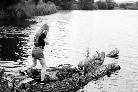 A young woman walks with a three month old Scottish Reed kitten near the lake in summer. The black-and-white photo was taken in the general plan in sunny weather with natural light