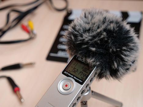 Record audio inside on a zoom h1 recorder with a dead cat in the studio in natural daylight. The background shows items such as Clapperboard, keyboard, cord, cable, 3.5, mini jack. You can use this photo in any project related to sound recording, podcast, recording studio, interview