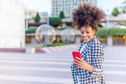 black afro woman looking happily to the phone while standing in the street