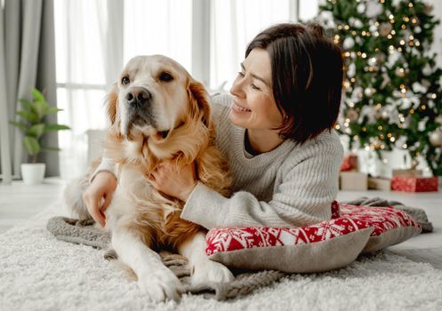 Girl with golden retriever dog lying on floor at home with Christmas tree. Young woman with pet doggy in festive time