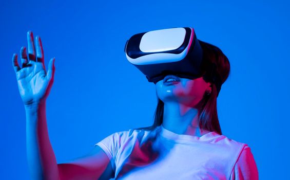 Woman touching air during the VR experience in neon light. VR headset. Woman using finger to touch on imaginary panel viewing on VR device