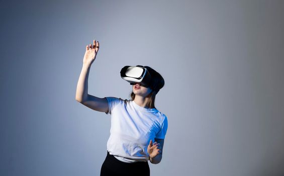 Close up of young woman stands in studio wearing VR glasses with a hand in air and trying to touch someting in virtual space. Virtual reality technology