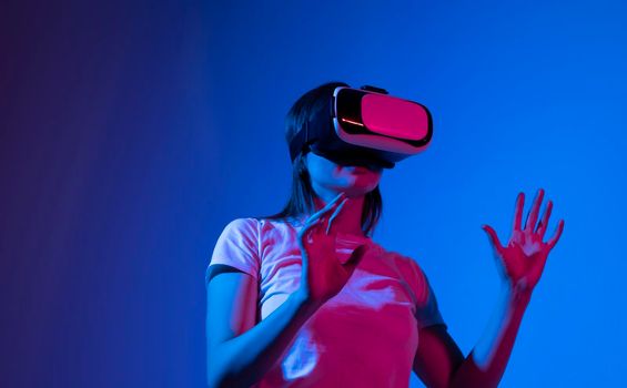 Young woman wearing VR headset while working with engineering project in lab with three dimensional printing in neon light studio. High tech engineering concept