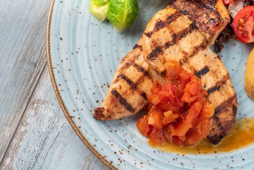 Grilled chicken breast in different variations with cherry tomatoes and different vegetables on wooden background