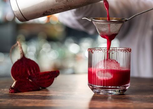 Alcoholic beetroot cocktail beverage in elegant glass on wooden table.