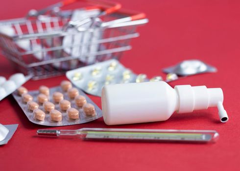 Spray, vitamins, Blister pack of pills , bottle lying near blurred mini basket on red background. Pharmacy Shopping Concept, copy space, banner. medicine background. High quality photo.