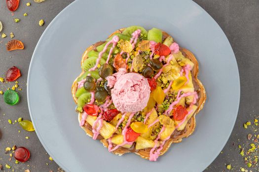 Heart waffle with kiwi and pineapple with gummy candy and ice cream on it.