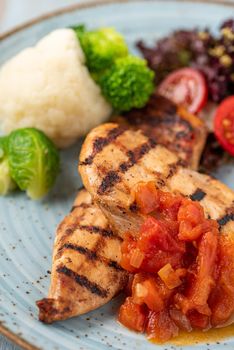 Grilled chicken breast in different variations with cherry tomatoes and different vegetables on wooden background