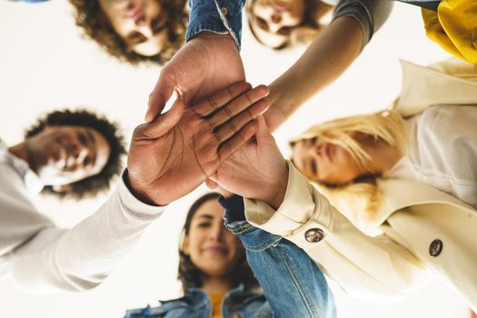 From below of group of content multiracial friends joining hands together and standing in circle