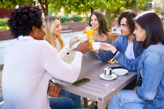 Multi-ethnic group of friends making a toast with their drinks while having a drink together at the outside table of a bar.