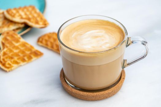 Cafe latte and heart waffles on marble table in the garden of the cafe