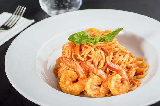 Pasta with jumbo shrimp on a white plate on a black background.