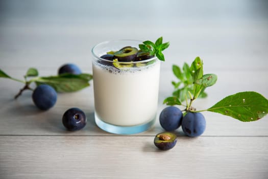 sweet homemade yogurt with fresh plum slices in a glass on a wooden table