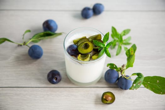 sweet homemade yogurt with fresh plum slices in a glass on a wooden table