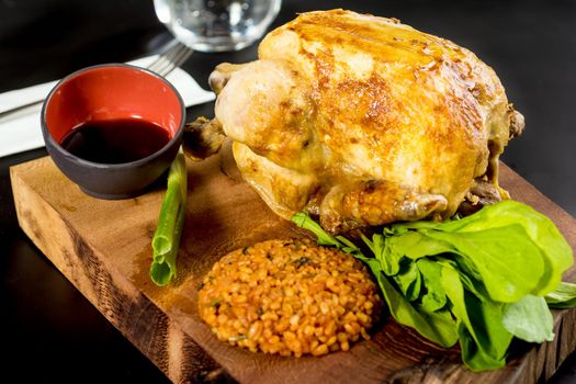 Roasted chicken cooked on charcoal with bulgur pilaf on a white porcelain plate.